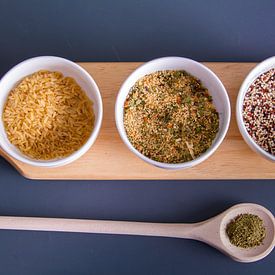 Houten plank met quinoa, rijst en couscous in witte schaaltjes - houten lepel met kruiden van Malu de Jong