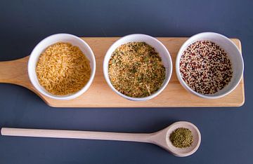 Houten plank met quinoa, rijst en couscous in witte schaaltjes - houten lepel met kruiden sur Malu de Jong