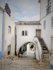 Alter Torbogen in einer Kopfsteinpflasterstraße in Óbidos, Portugal von Hecate Pim