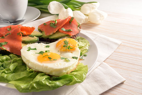 Urlaubsfrühstück mit Liebe, Spiegeleier in Herzform, Sandwiches mit Avocado und Räucherlachs auf Sal