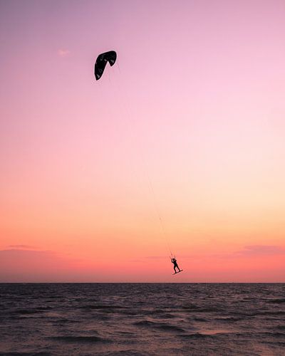 Kitesurfer zweeft boven zee tijdens roze zonsondergang