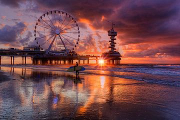 Pier von Scheveningen und zwei Surfer, die sich bei Sonnenuntergang im nassen Sand spiegeln