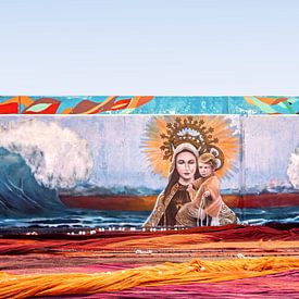 Graffitimuur met gekleurde visnetten ervoor te drogen op de kade van Los Abrigos op Tenerif. van Stephaniek Putman