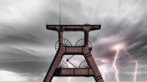 An old disused winding tower in front of impressive lightning bolts in the sky