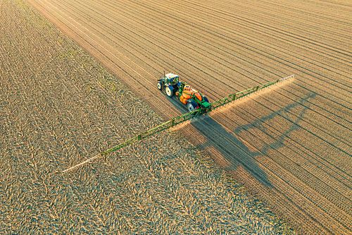 Tractor met veldspuit in een veld gezien van bovenaf