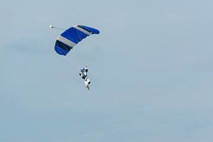 Parachutist aan een blauwe parachute tegen een licht blauwe achtergrond
