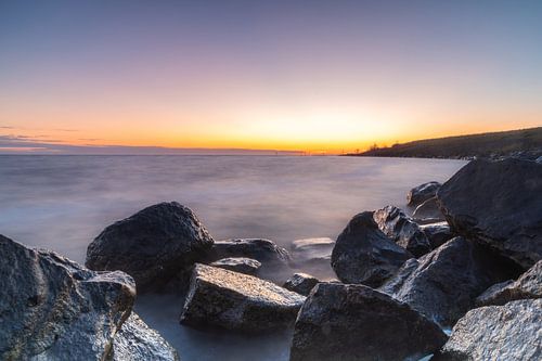Tussen de rotsen de zon zien opkomen aan het IJsselmeer