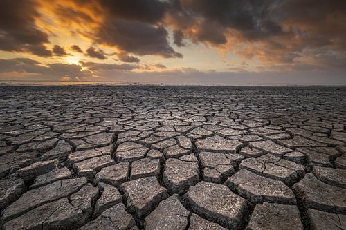 Droogte aan het wad onder een dreigende lucht tijdens zonsondergang