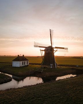 A Dutch windmill at sunset in a polder landscape by Ewold Kooistra