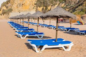 Rijen met strandparasols en blauwe ligbedden op strand in Albufeira Portugal van Ben Schonewille