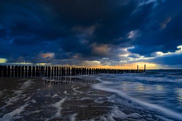 Hollandse wolkenlucht en typische golfbreker van houten palen langs de Zeeuwse kust