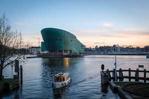 Een boot vaart voor Nemo in Amsterdam bij het Oosterdok met een licht gele wolkenlucht van Bart Ros