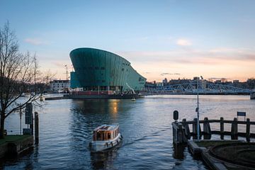 Een boot vaart voor Nemo in Amsterdam bij het Oosterdok met een licht gele wolkenlucht