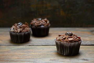 three chocolate cupcakes with cocoa butter cream on dark wood, one is in focus, copy space, narrow d by Maren Winter