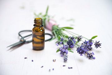 lavendelbloemen, een flesje met essentiële kruidenolie en een schaar op wit geschilderd hout, kopiee van Maren Winter