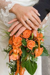 Mains d'un couple de mariés sur le bouquet de la mariée