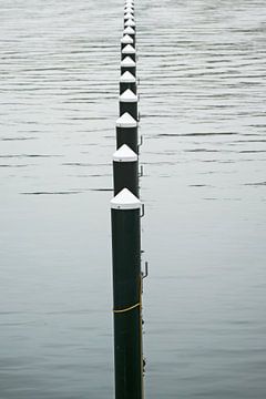 Row of black mooring piles or dolphins in the water, empty yacht by Maren Winter