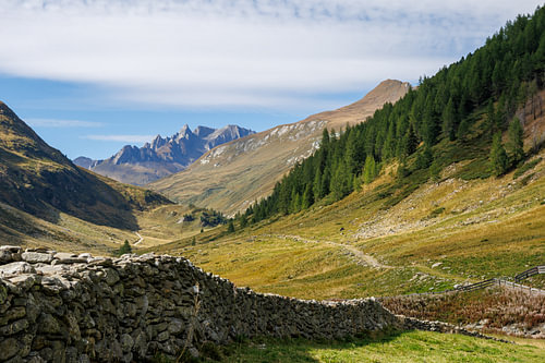 Trail through the high Alpine valley with a historic stone wall