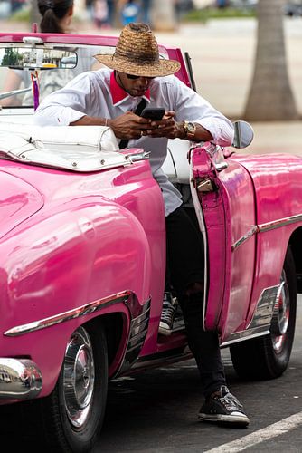 Man met mobiele telefoon in roze oldtimer in Havana