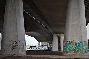 Un cargo navigue sous un pont en béton avec des piliers sur Maud De Vries