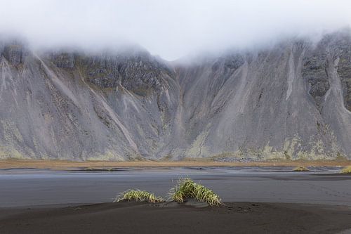 desolate lava beach with clouds around mountains
