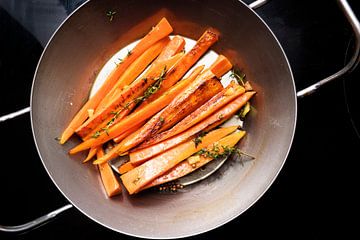 wortelgroenten, geglazuurde wortelen met tijm, gember en honing in een ijzeren pan op het zwarte for van Maren Winter