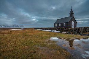 Ein bewölkter Wintertag in der schwarzen Kirche in Budir, mit einer Spiegelung der Kirche im See vor