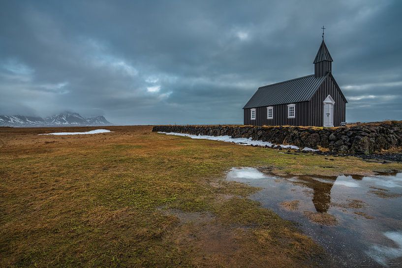 A cloudy winter day at the black church in Budir, with a reflection of the church in the lake in fro by Anges van der Logt