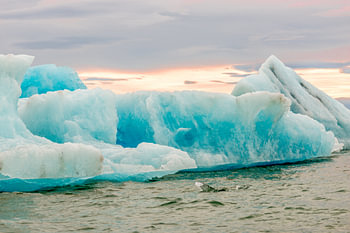 Big ice floes in Jökulsárlón ice lake in Iceland with their typical deep blue color against an orang