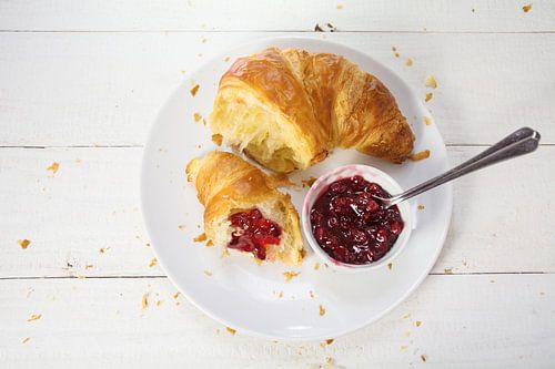 verse croissant met rode cranberryjam voor het ontbijt op een bord op een witte houten tafel, uitzic