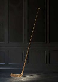 A vintage wooden ice hockey stick standing upright in a dark room by Morgan