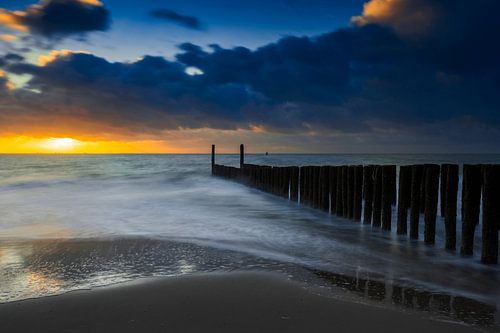 Hollandse wolkenlucht en typische golfbreker van houten palen langs de Zeeuwse kust