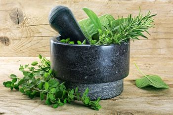 fresh mediterranean herbs, oregano, rosemary and sage in a mortar made of black granite on a rustic 