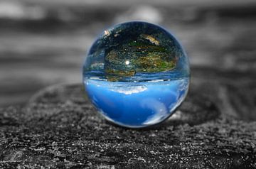 Glazen bol op het strand van de Oostzee. Zwart-wit foto met een gekleurde glazen bol waarin het land van Martin Köbsch