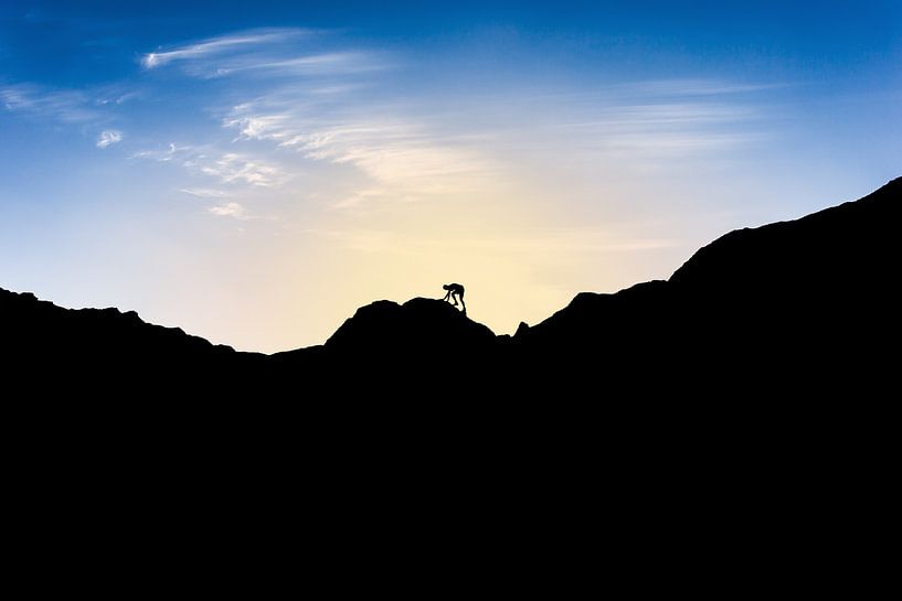 Silhouette d'un homme escaladant une montagne au coucher du soleil. Wout Kok One2expose par Wout Kok