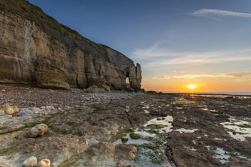 Ruwe kust van Normandië met kalkstenen rotsformaties, getijdenpoelen en groen zeewier tijdens een rustige zonsondergang aan de Atlantische kust van Frankrijk
