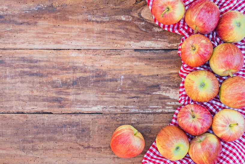 Many red apples on rustic wooden table top view with red checkered tablecloth and copy space by Alex Winter