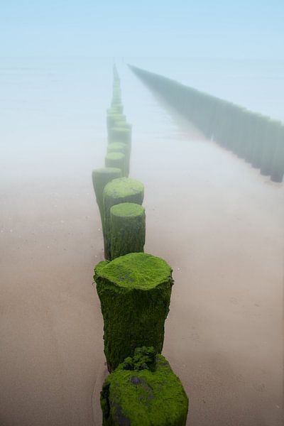 Golfbreker in de mist aan het strand van de kust in Zeeland van Wout Kok