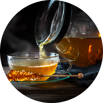 Hete dampende thee wordt uit een pot in een glazen kop gegoten, geserveerd met een stokje van rots s van Maren Winter