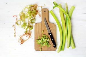 rabarberstelen en spiralen van de rabarberhuid, gesneden stukken en een keukenmes op een snijplank, 