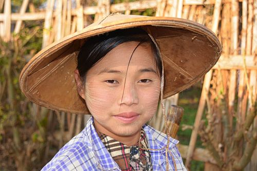 Portrait of a girl with a tanaka and a straw hat in rural Myanmar