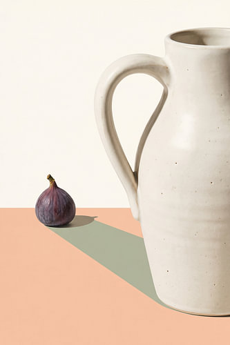 A minimalist still life featuring a ceramic jug and a fig
