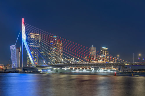 Le pont Erasmus illuminé en rouge, blanc et bleu, avec la ligne d'horizon de Rotterdam en arrière-pl sur MS Fotografie | Marc van der Stelt