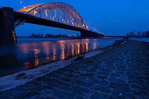 Brug over de rivier de Waal naar Lent van Nijmegen tijdens het ochtendgloren met donkerblauwe lucht 