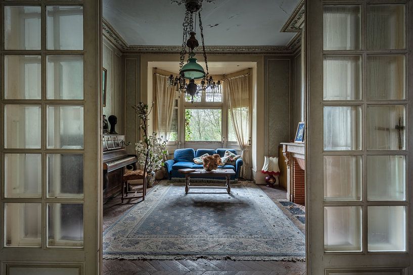 Living room with blue sofa and piano in abandoned house by Inge van den Brande
