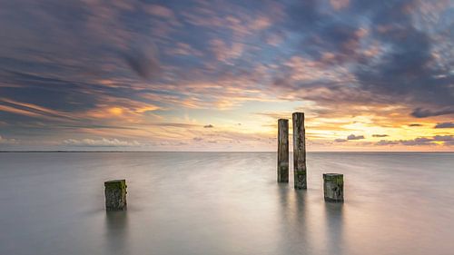 Palen in de waddenzee tijdens zonsondergang
