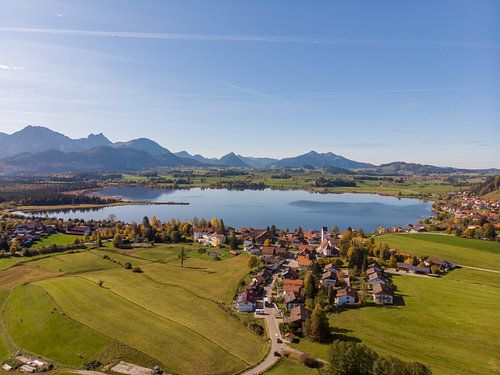 Luftbildpanorama vom Hopfensee mit Alpen und blauem Himmel im Hintergrund