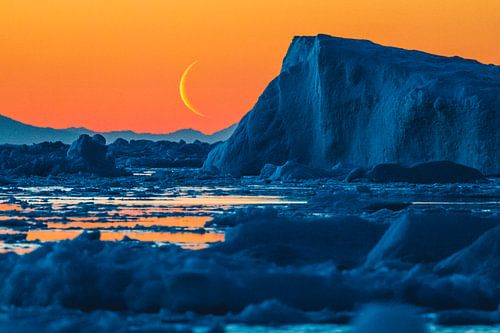 Opkomende maan boven ijsschots bij oranje zondersondergang