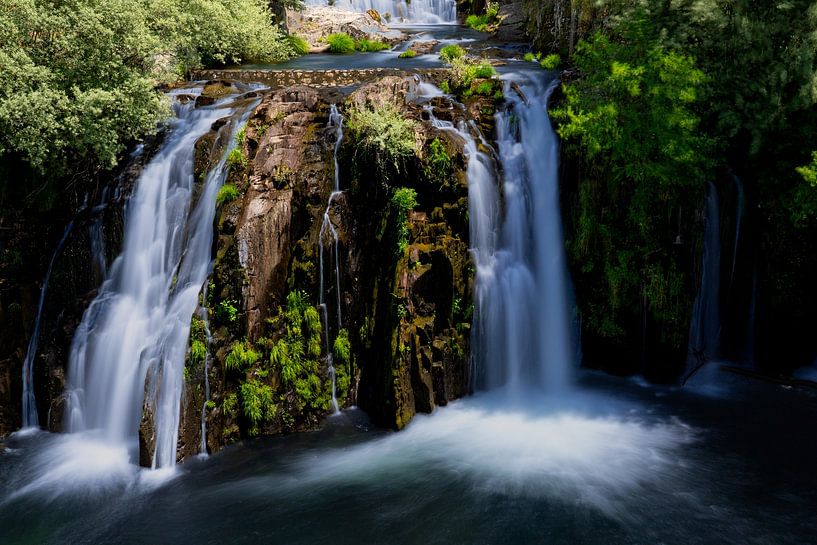 A majestic waterfall cascading down over rugged, moss-covered rocks. by Wolbert Erich