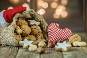 Christmas heart with nuts and star shape cookies in Santa Claus bag with red cap on wooden table by Alex Winter